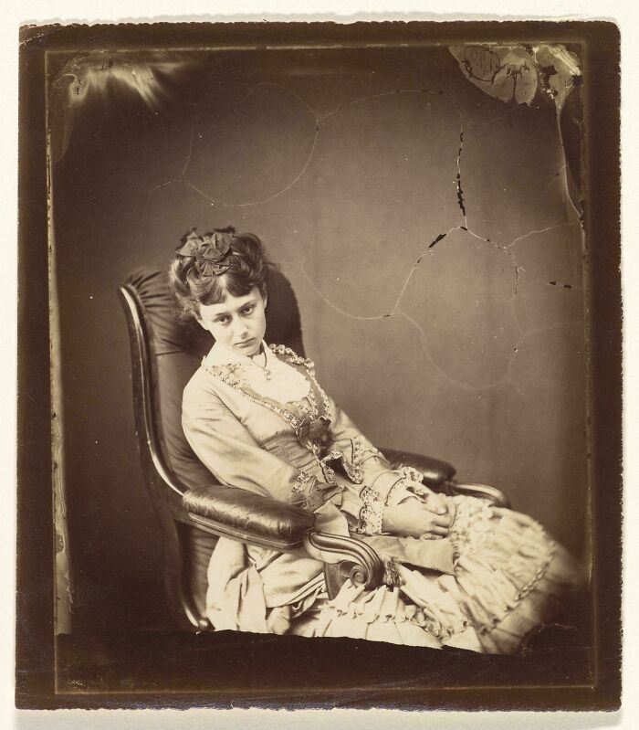 Victorian era woman in elegant dress sitting on a chair, showcasing vintage fashion and style.