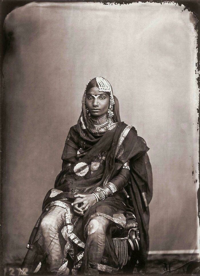 Victorian era woman in traditional attire with intricate jewelry, seated, offering a glimpse into historical fashion.