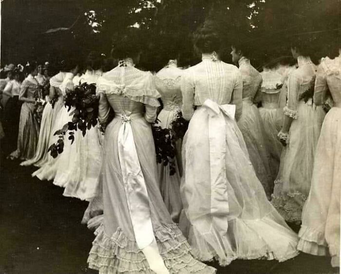 Victorian era women in elegant dresses, walking in a procession, showcasing historical fashion.