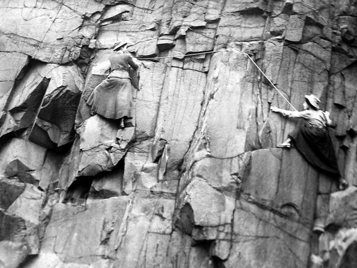 Victorian era women rock climbing in long skirts, showcasing unique historical activities.