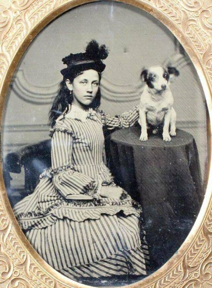Victorian era girl in striped dress, posing with a dog on a table, captured in an ornate photo frame.