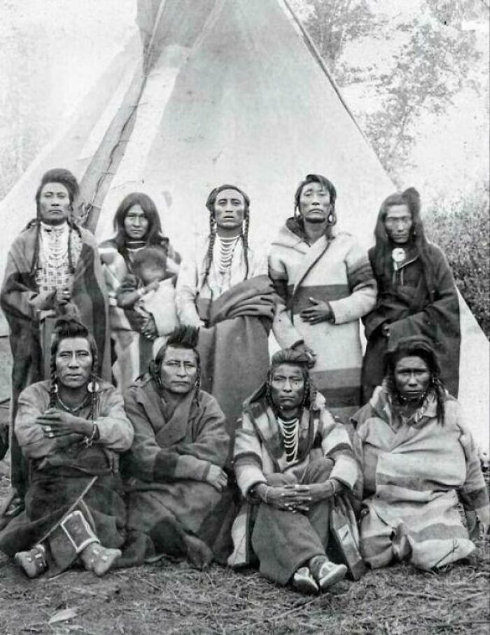 Group of Native Americans in traditional clothing in the Victorian era, in front of a tipi.