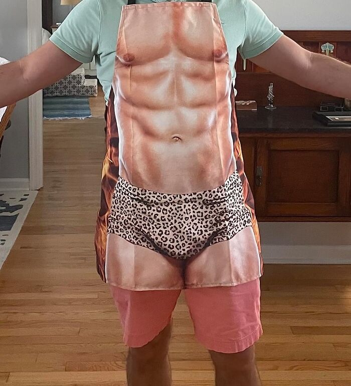 Man wearing a funny apron with a muscular body print, featuring leopard-print shorts.