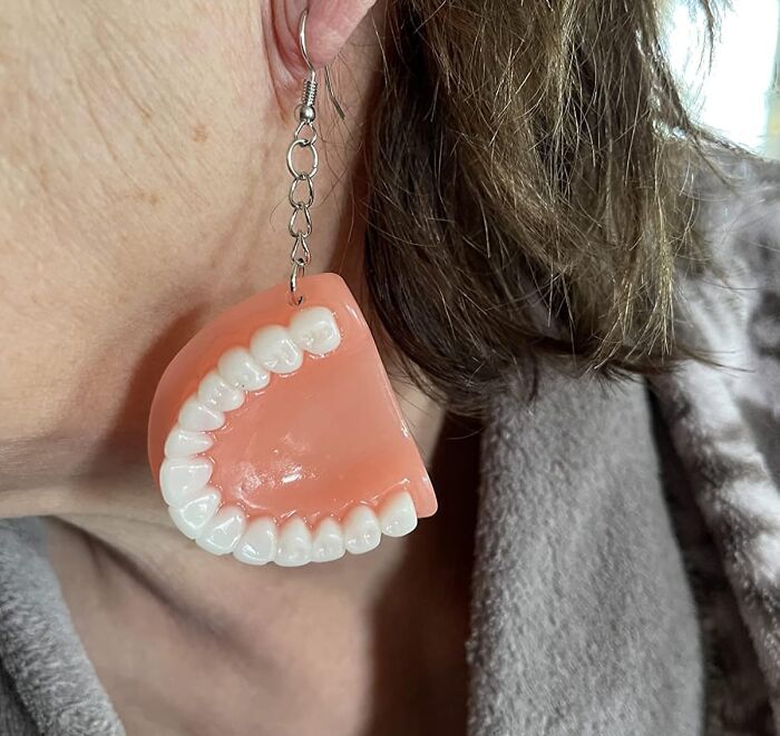 Earring shaped like a set of teeth, a funny Amazon find, worn by a person with brown hair.