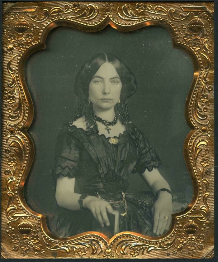 Victorian era woman in dark dress, adorned with jewelry, captured in an ornate gold frame.