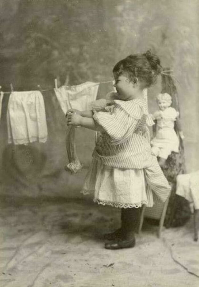 Victorian era child in striped dress hanging laundry, with vintage clothing in the background.