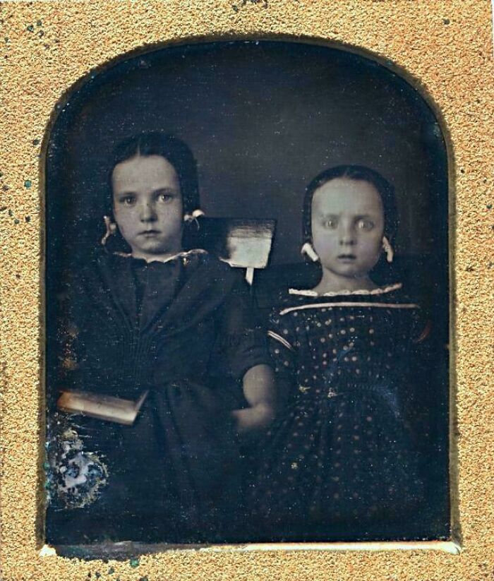 Two Victorian-era children in formal attire, seated against a dark backdrop, capturing the fashion of the time.