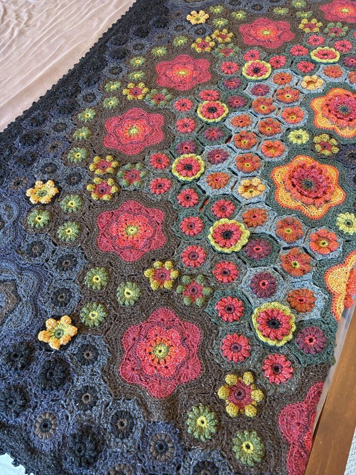 Colorful crochet masterpiece featuring detailed floral patterns in various warm and cool tones on a textured fabric background.