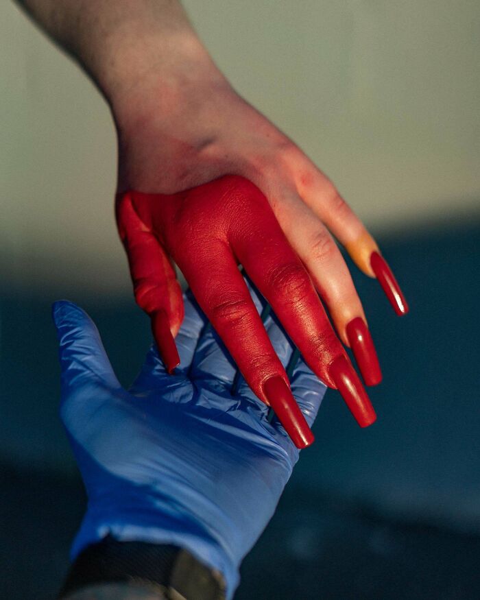 Hand with long red nails painted red held by hand in blue medical glove, an example of awful taste but great e*******n.