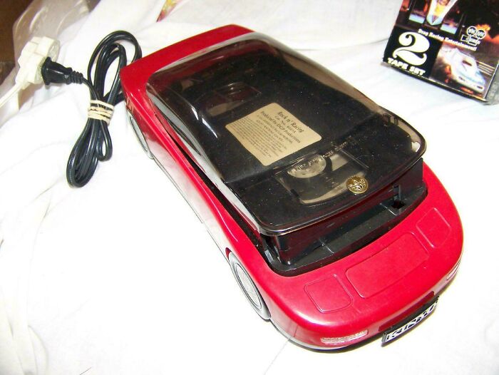 Red car-shaped cassette tape player with black lid and power cord, a nostalgic photo from vintage electronics collection.