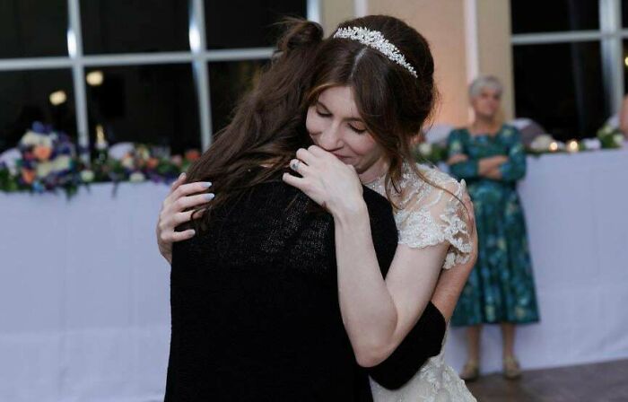 Bride hugging a guest heartfelt at reception, with another guest in the background, highlighting wedding atmosphere.