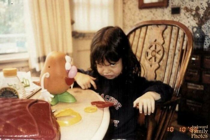 Child making a funny face at the table with a Mr. Potato Head toy, capturing an awkward family photo moment.