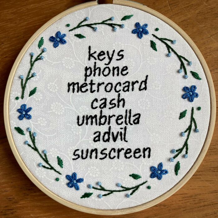 Embroidered reminder list with blue flowers and green vines on white fabric showcasing embroidery skills.