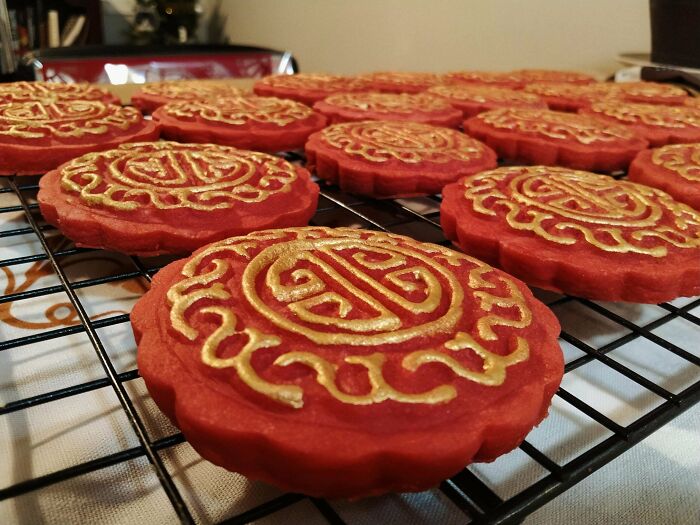 Red cookies with intricate golden designs cooling on a wire rack, showcasing incredible bakes with detailed decorative patterns.