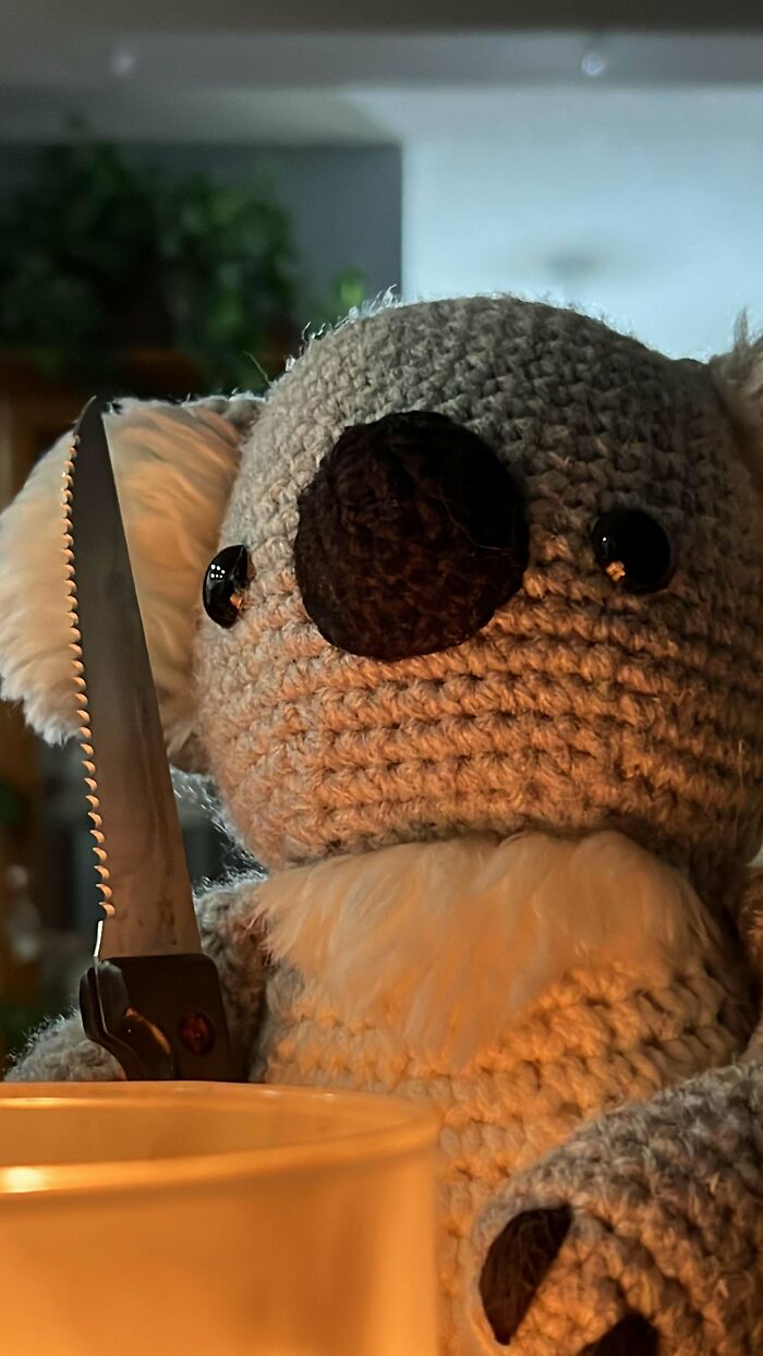 Crochet stuffed koala holding a serrated knife, highlighting creative crochet masterpieces in a cozy home setting.