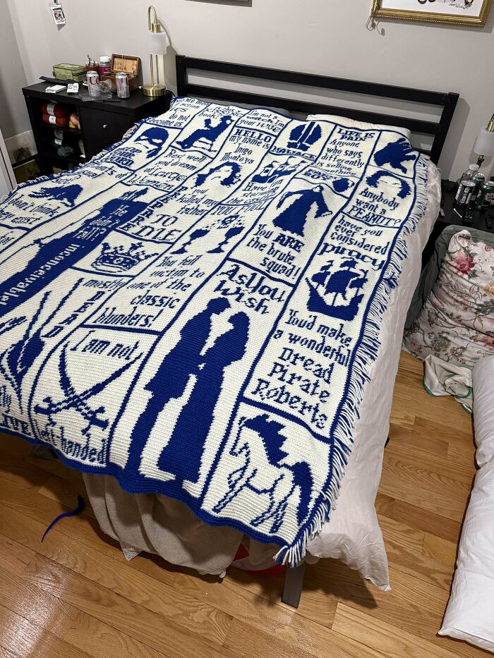 Blue and white crochet blanket with detailed patterns and quotes laid out on a bed in a bedroom setting.