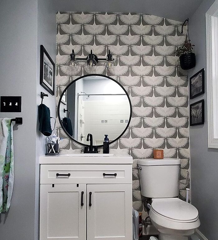 Small bathroom with patterned wallpaper, circular mirror, vanity, and modern light fixture, suitable for not-handy DIYers.