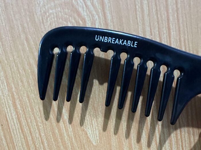 Black comb labeled "unbreakable," missing several teeth, on a wooden surface; example of low-quality item.