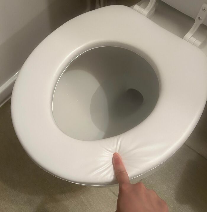 Low-quality toilet seat being pressed with a finger, showing its poor material quality.
