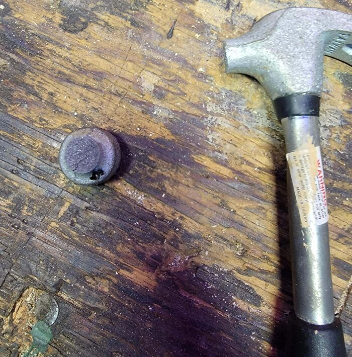 Low-quality hammer with detached head lying on a wooden surface.