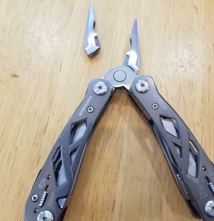 Broken multitool on a wooden table, showing low quality item failure with a snapped blade.