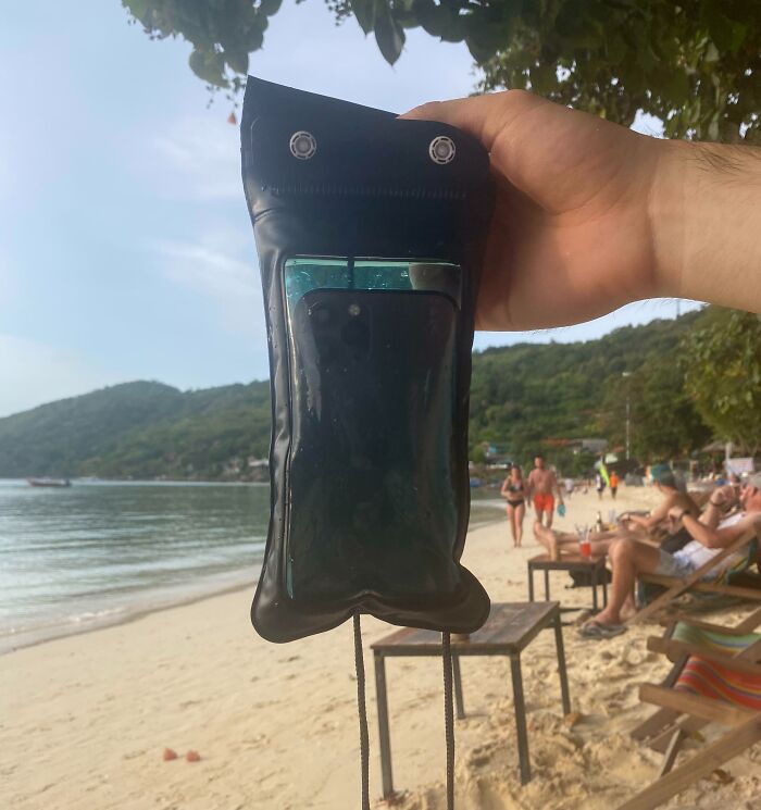 Low-quality item: a flimsy phone case held on a beach, with people relaxing in the background.