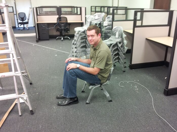Man sitting uncomfortably on a broken chair in an office, highlighting low-quality items people bought.