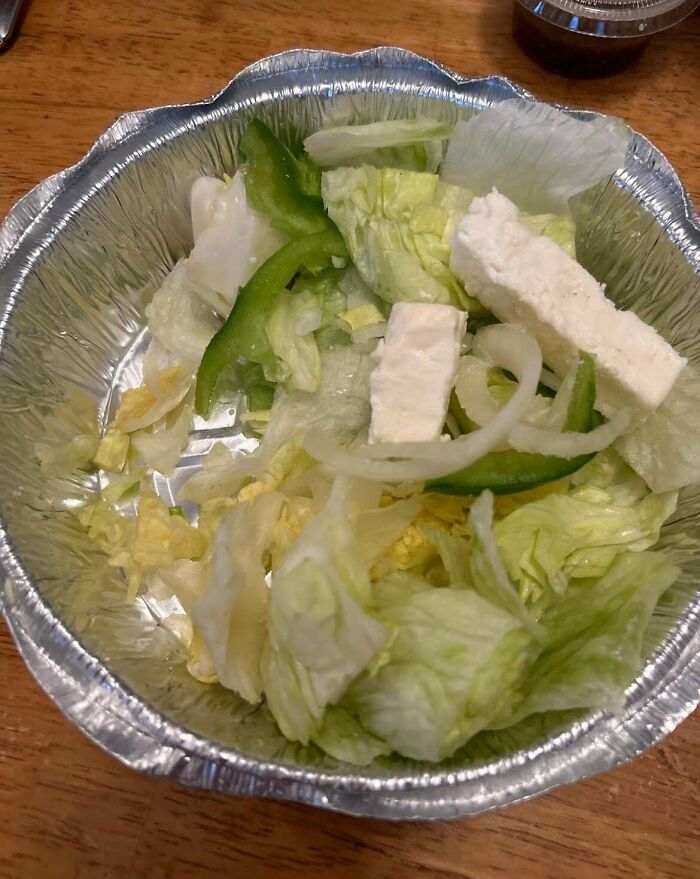 Sparse salad in a foil container, highlighting infuriating food scams with minimal lettuce, onion, and cheese.