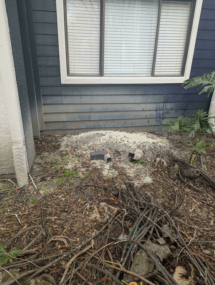 Broken drainage pipes and trash dumped near a house wall, showcasing neighbors being so horrific they had to be shamed.