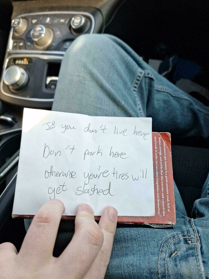 Hand holding a warning note from terrible neighbors about parking in a car.