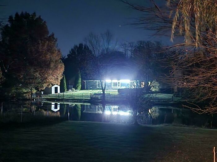 House with bright lights reflecting on a pond at night, an example of neighbors causing disturbance to others nearby.