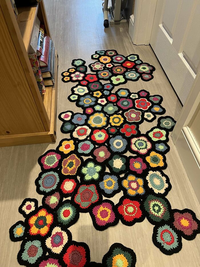 Colorful crochet masterpiece rug with floral patterns laid out on a wooden floor in a hallway.