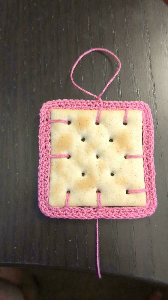 Square cracker threaded and framed with pink crochet yarn on a dark wooden surface in a crochet masterpiece project.