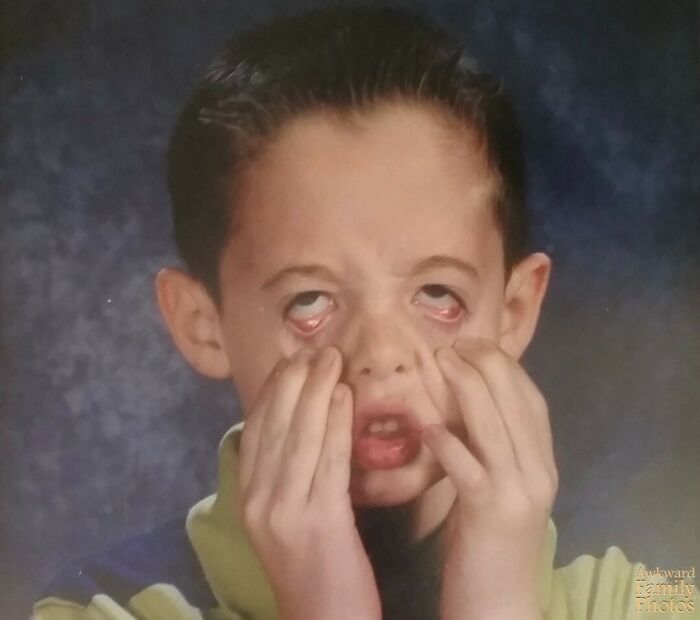 Young boy making a funny face in an awkward family photo with a blurry gray backdrop and casual clothing.