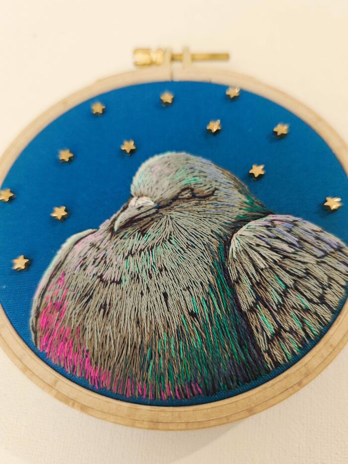 Colorful embroidery of a resting bird with detailed feathers on blue fabric, showcasing incredible embroidery skills.
