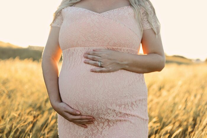 Pregnant woman in a field wearing a lace dress, holding her belly, possibly related to secret affairs of teachers.