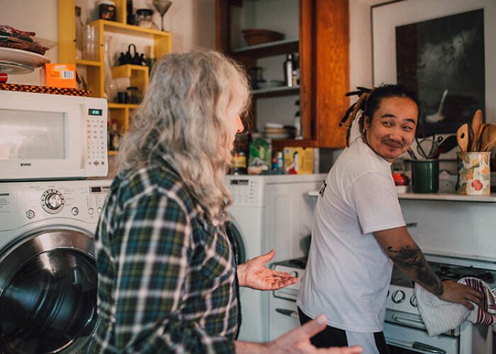 Two people in a kitchen sharing surprising life hacks, one cooking, the other gesturing near a washer-dryer.
