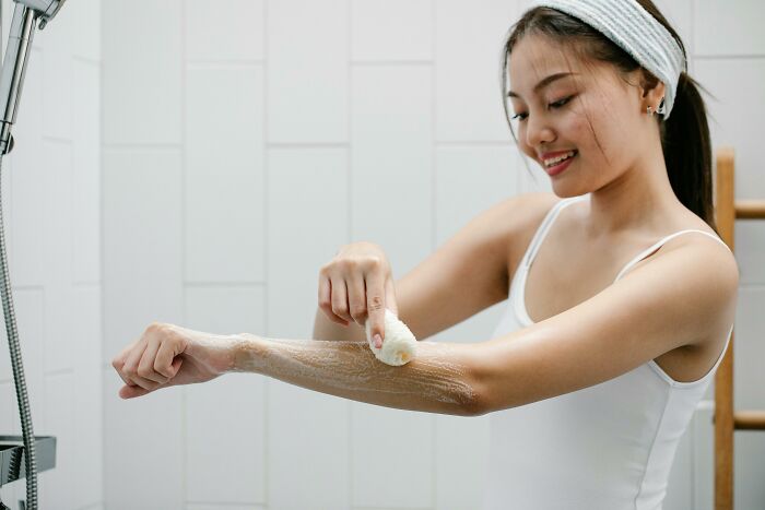 A woman in a bathroom smiling and applying a skincare product to her arm, highlighting everyday things that might seem harmless.