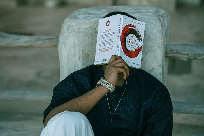 Person sitting and covering face with a book, pondering adult realizations similar to discovering Santa isn't real.