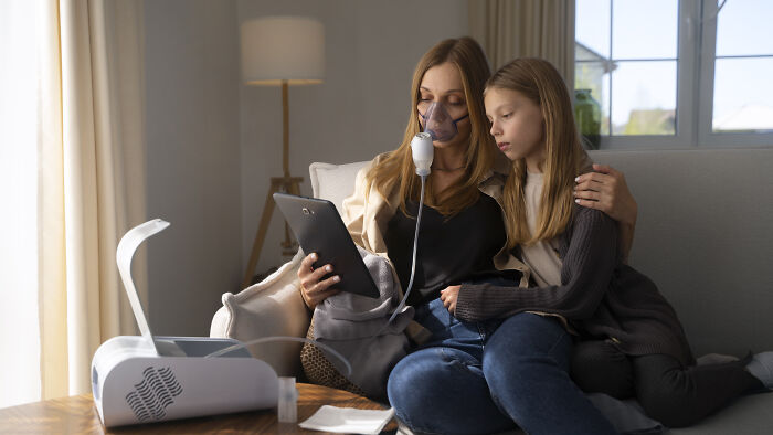 Woman using a nebulizer and tablet, with a child sitting beside her, showing lifestyle improvement.