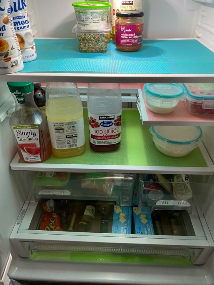 Organized fridge with juice bottles, containers, and pantry staples on colorful shelf liners.