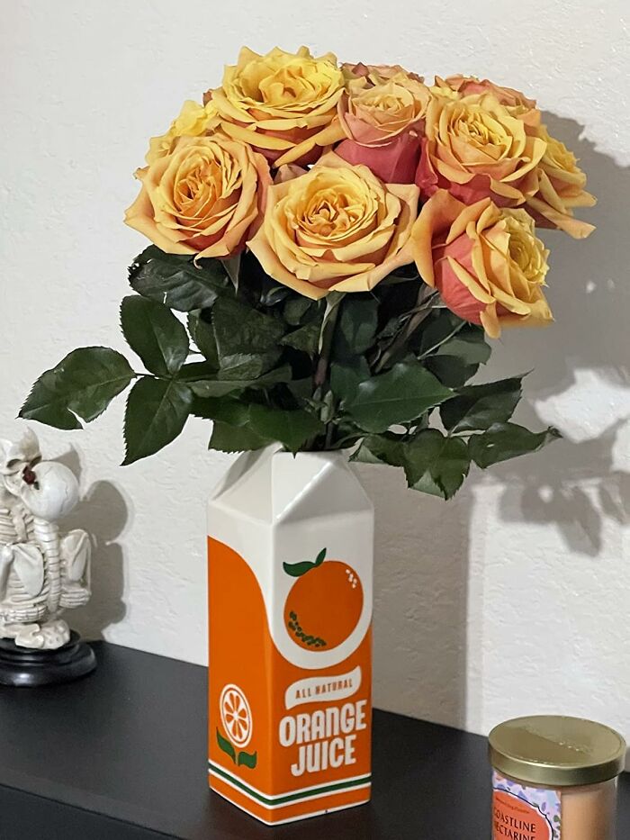 Retro Fever: Yellow roses in a vintage orange juice carton vase on a black shelf.