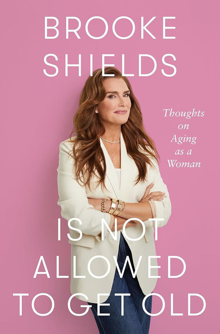 Brooke Shields in a white blazer, posing against a pink background, discussing aging and personal revelations.