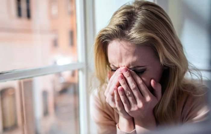 A distressed woman crying by a window, representing guilt and emotional struggle over adoption decision.