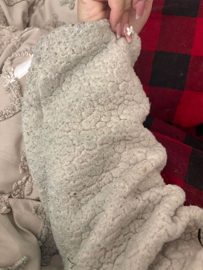 Close-up of a textured white blanket with a woman's hand holding it, suggesting recent stains in a home setting.