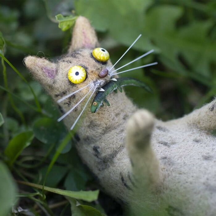 Funny-looking art doll of a wide-eyed cat crafted by a Georgian artist, lying in grass.
