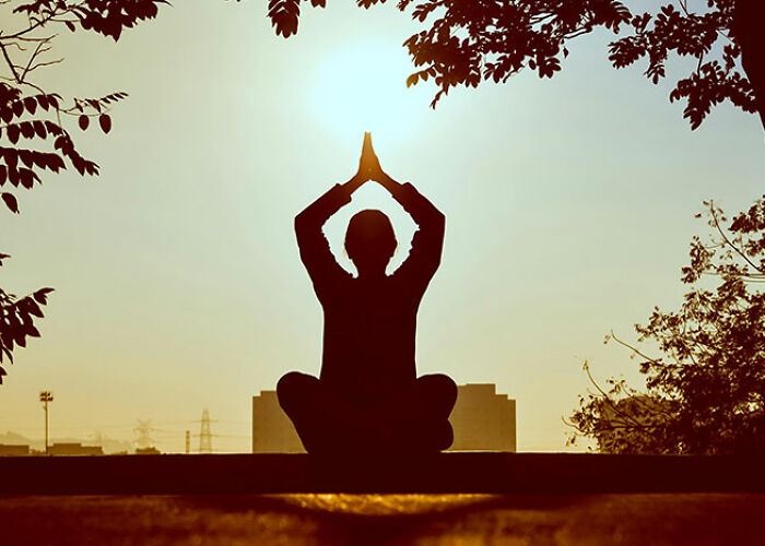 Person meditating outdoors at sunrise, practicing a life hack for mindfulness.