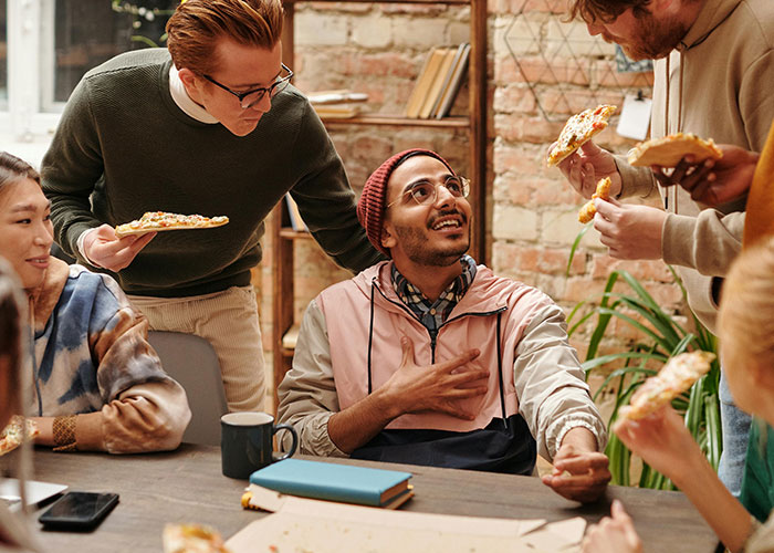Group of friends sharing pizza and laughing, capturing a moment of someone being different and thoughtful.