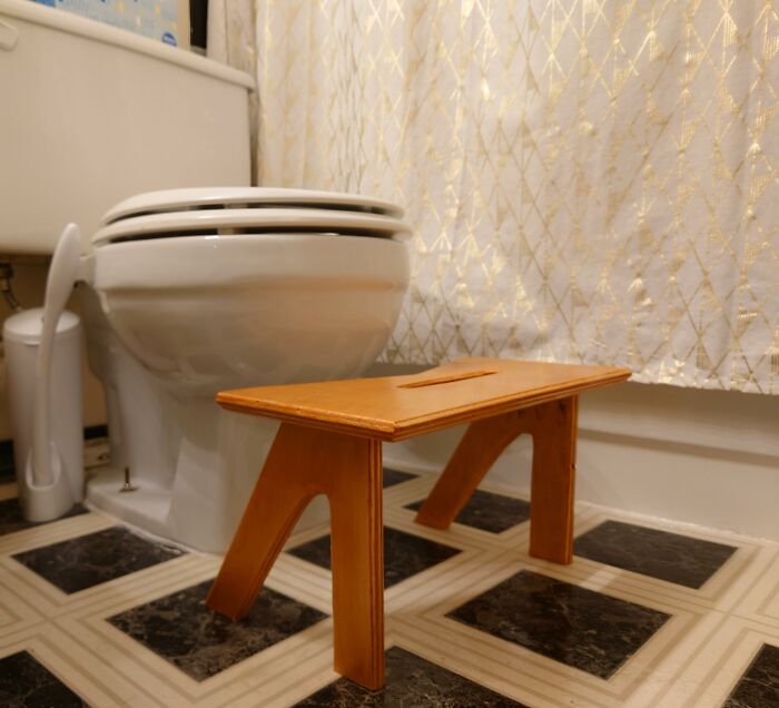 Bathroom with a small wooden stool in front of a toilet.