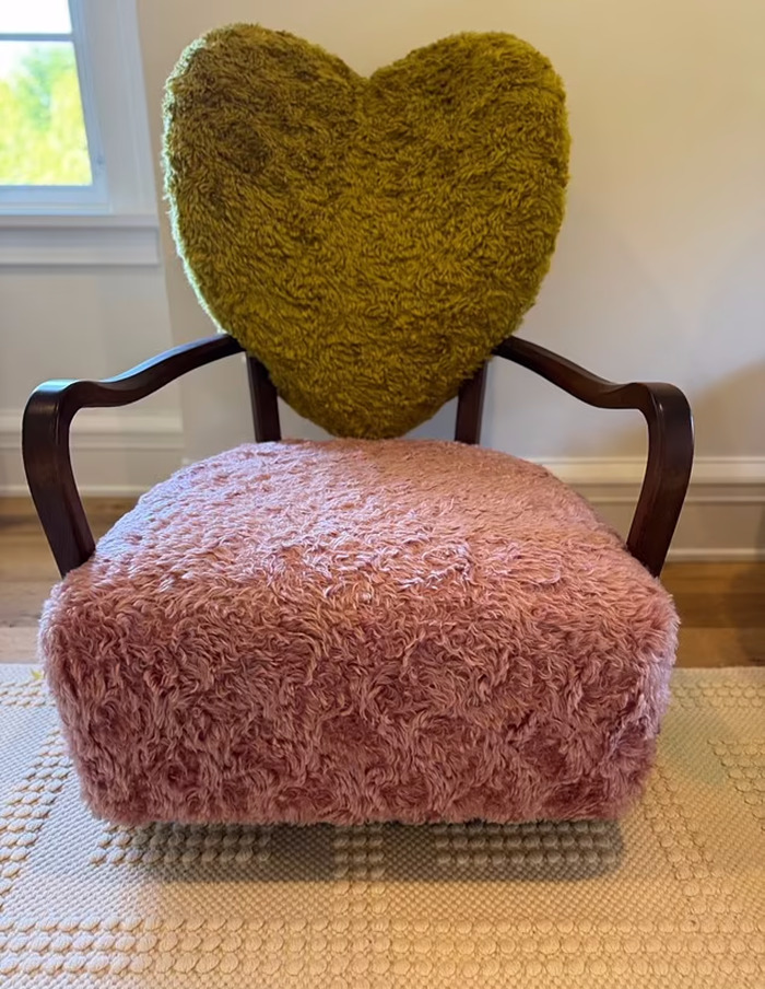 Plush chair with heart-shaped cushion, once owned by a luxury influencer, showcased in a bright room.